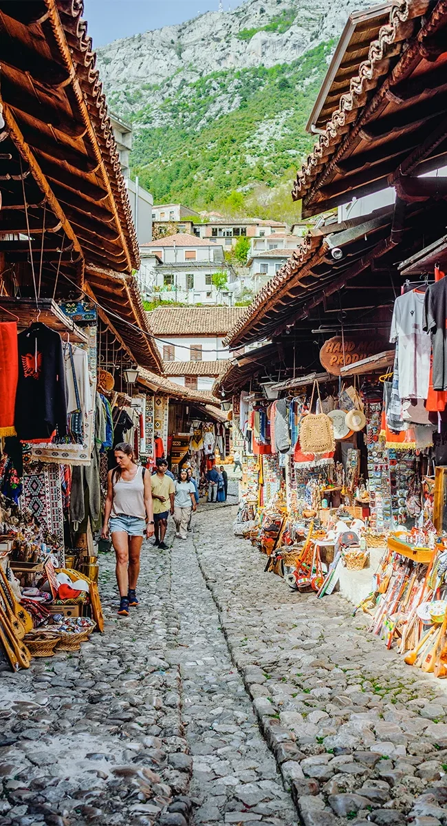 Ein albanisches Bergdorf mit traditionellen Häusern, vor denen sich albanische Marktstände aneinanderreihen.