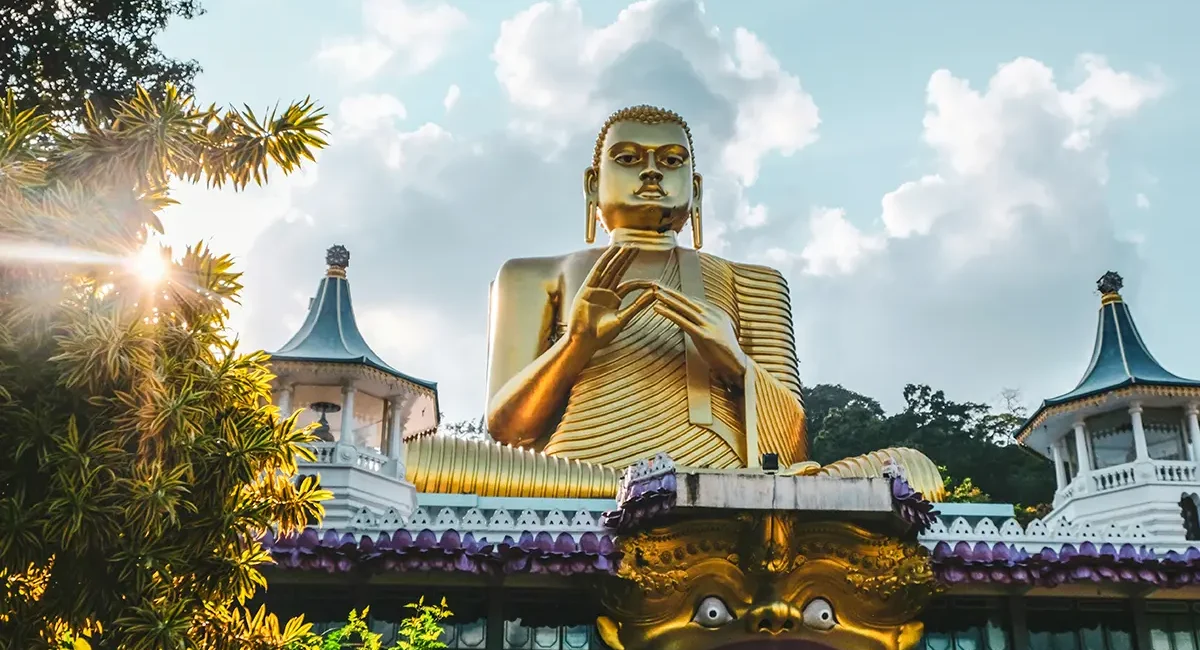 Eine sehr große, goldene Buddha-Statue sitzt auf dem Dach des Goldenen Tempels von Dambulla in Sri Lanka.