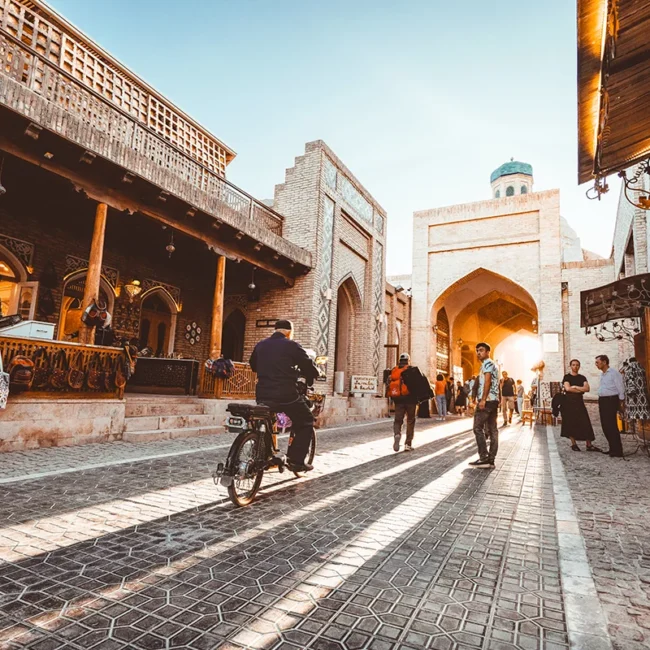 Eine lebendige Straße in der Altstadt von Buchara in Usbekistan mit historischen Gebäuden und dem Stadttor.