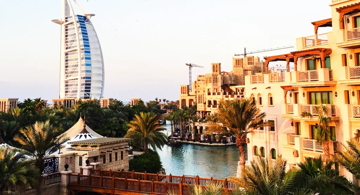 Blick auf Dubai mit dem ikonischen Burj Al Arab Hotel im Hintergrund, umgeben von luxuriösen Hotels, Wasserwegen und Palmen.