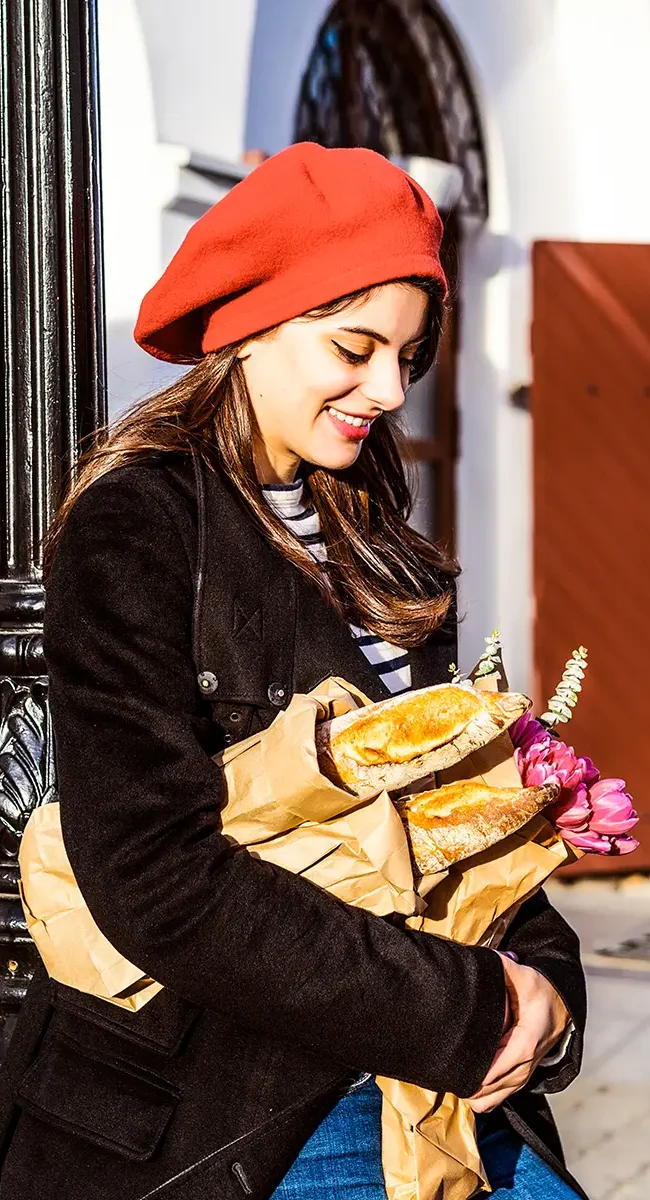 Eine Französin mit roter Baskenmütze, die eine Tüte mit Baguette trägt