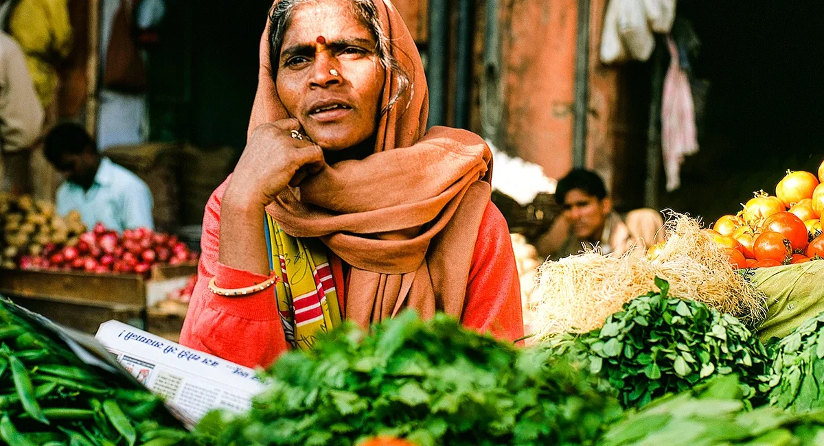 Eine indische Marktfrau, die inmitten eines geschäftigen Gemüsemarktes in Indien sitzt und ihre Waren verkauft.