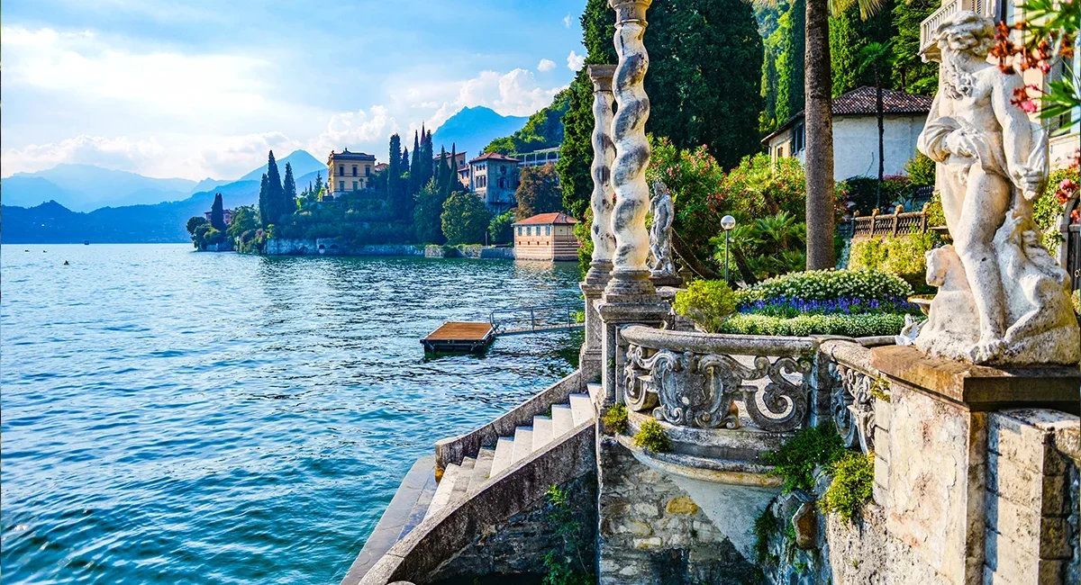 Die Villa Monastero am Comer See in Italien liegt direkt am Wasser, mit einer Steintreppe zum See und Bergen im Hintergrund.