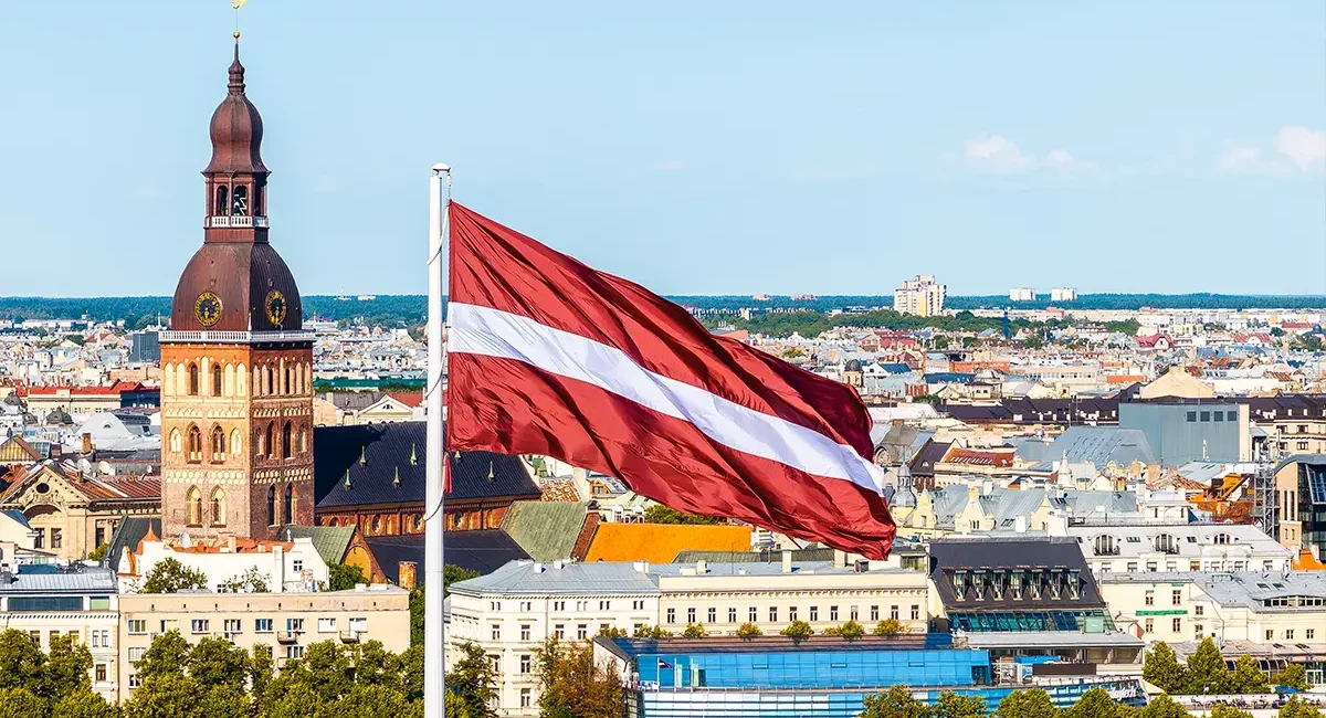 Eine Luftaufnahme der Altstadt von Riga, Lettland, mit der lettischen Flagge im Vordergrund und dem Dom zu Riga im Hintergrund.