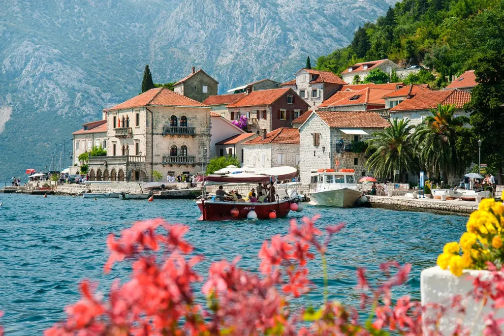 Die malerische Küstenstadt Perast in der Bucht von Kotor, Montenegro, mit ihren rot gedeckten Gebäuden, Booten im klaren Wasser und Bergen im Hintergrund.