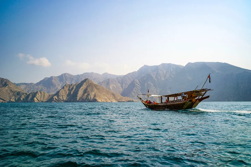 Eine traditionelle Dhau bei einer Bootsfahrt durch die fjordähnlichen Gewässer im Oman, umgeben von schroffen, kargen Bergen.