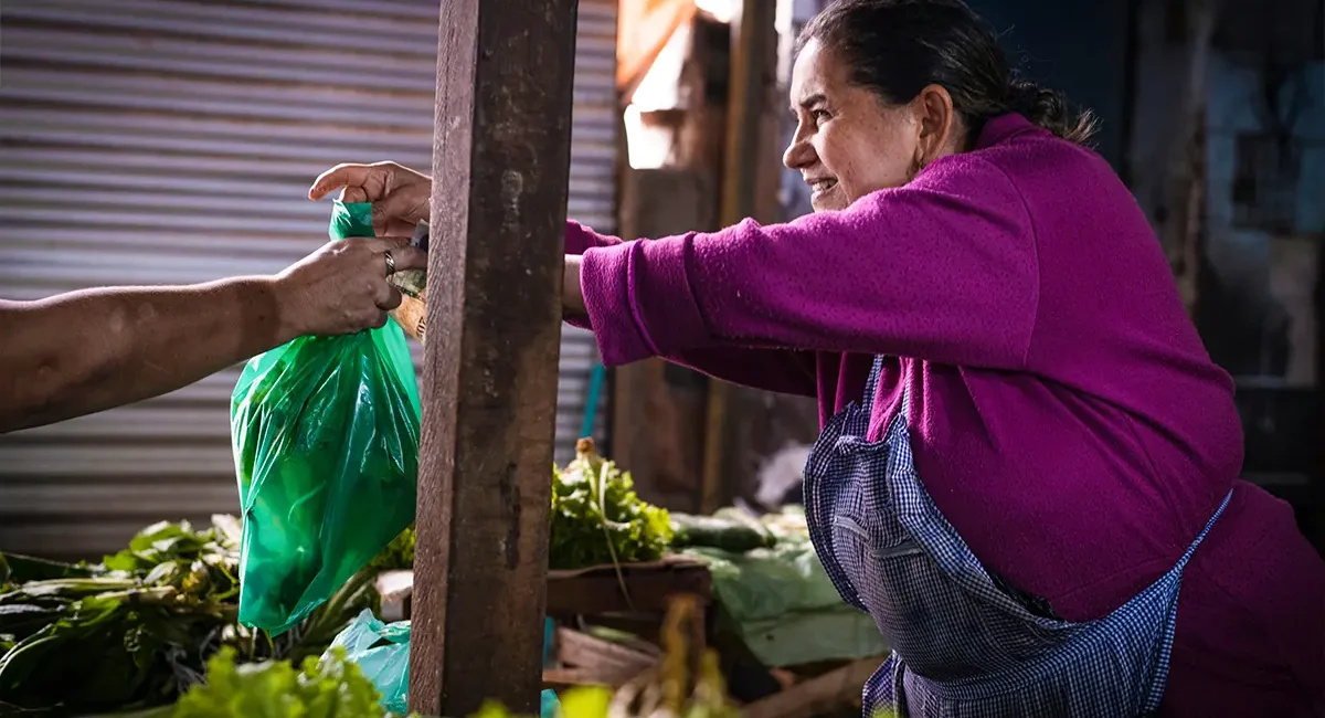 Eine Marktfrau verkauft in Paraguay frisches Gemüse und übergibt die Ware an einen Kunden.