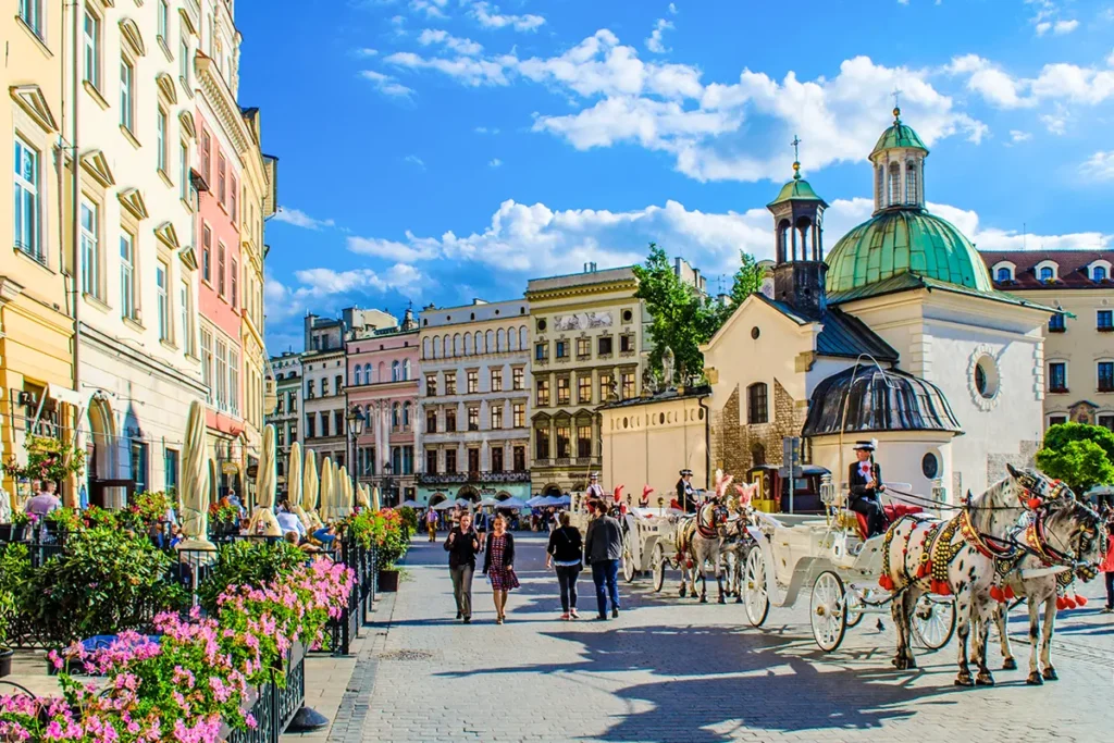 Der Hauptmarktplatz in Krakau, auf dem mehrere prachtvolle Pferdekutschen vor einer Kirche und historischen Gebäuden stehen.