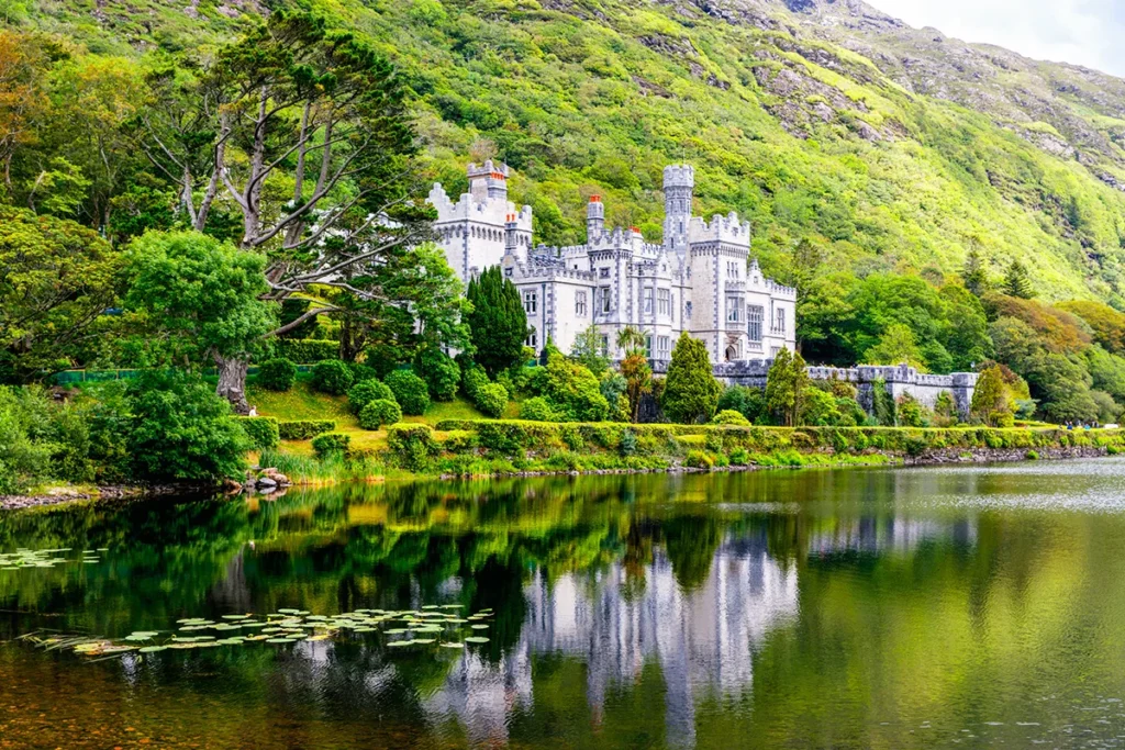 Die neugotische Kylemore Abbey, die malerisch am Ufer eines Sees vor der grünen Bergkulisse in Irland liegt.