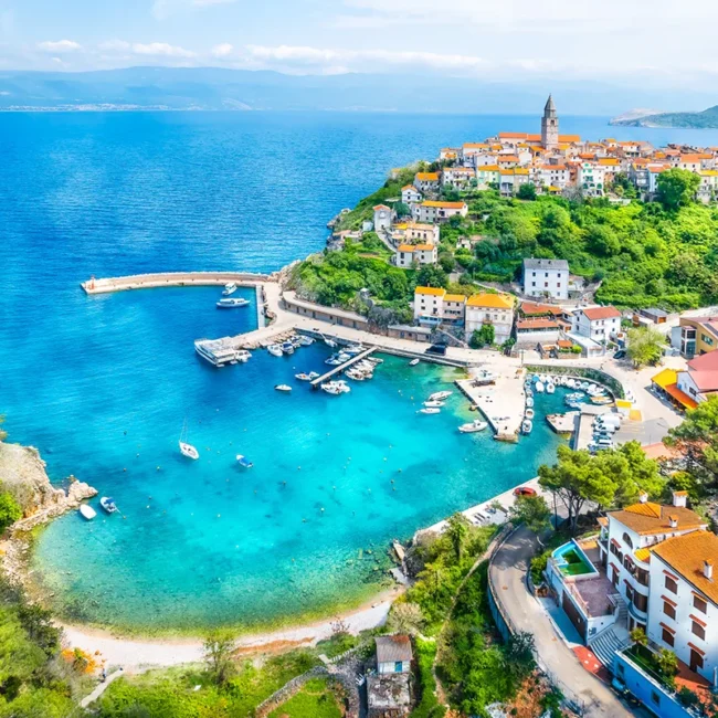 Der Ort Vrbnik auf der kroatischen Insel Krk, mit Blick auf seinen türkisfarbenen Hafen und die umliegende Adria.