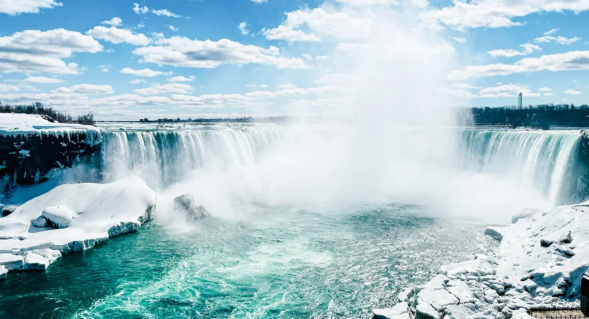 Die teilweise vereisten Niagarafälle inmitten einer verschneiten Winterlandschaft unter einem strahlend blauen, leicht bewölkten Himmel in Ostkanada.