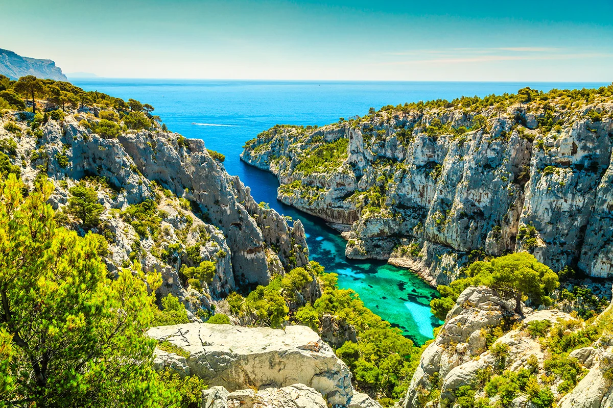 Die Calanque d'En-Vau, eine tief eingeschnittene Meeresbucht im südfranzösischen Nationalpark Calanques, die von steilen, hellen Kalksteinfelsen und üppiger grüner Vegetation umgeben ist.