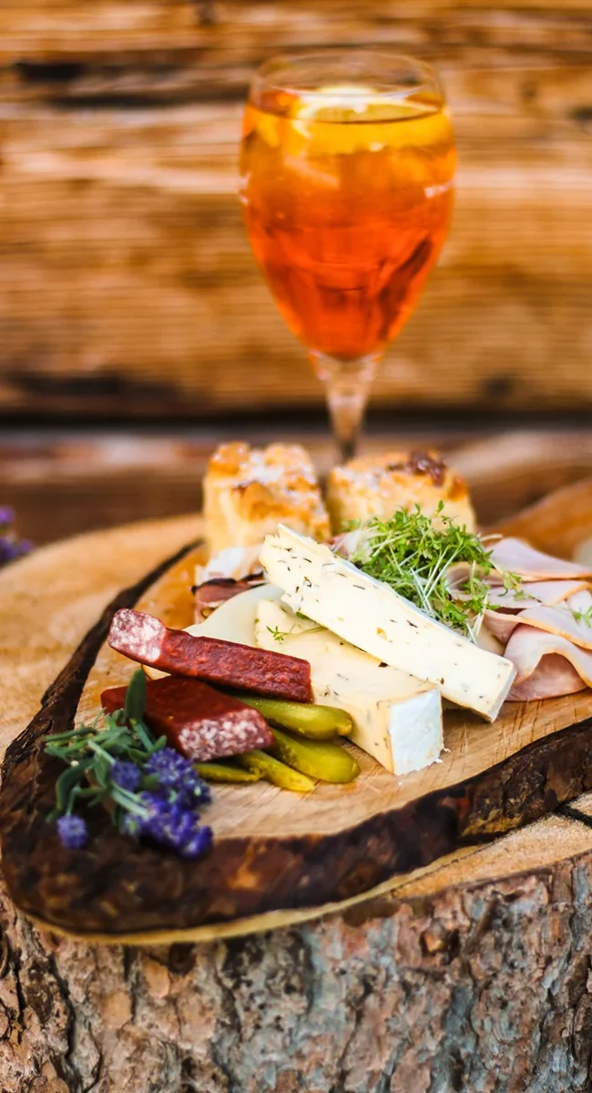 Ein Vesperbrett mit frischem Käse, Wust, Kuchen und einem Glas Aperol in Südtirol.