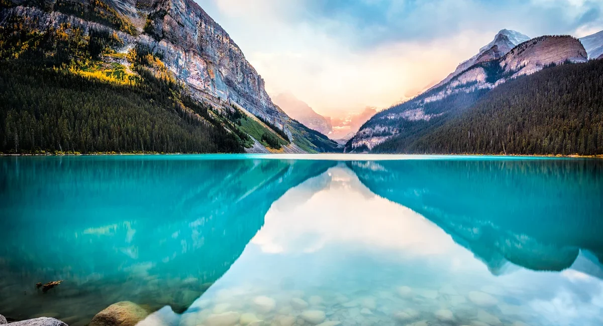 Der türkisblaue Lake Louise im kanadischen Banff-Nationalpark, wie er sich bei Sonnenaufgang spiegelglatt vor den schneebedeckten Gipfeln der Rocky Mountains präsentiert.