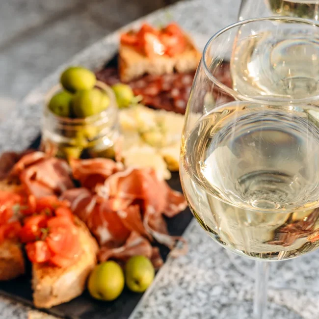 Vesper mit Baguette, Tomaten und Schinken auf einem Teller angerichtet, dazu Wein