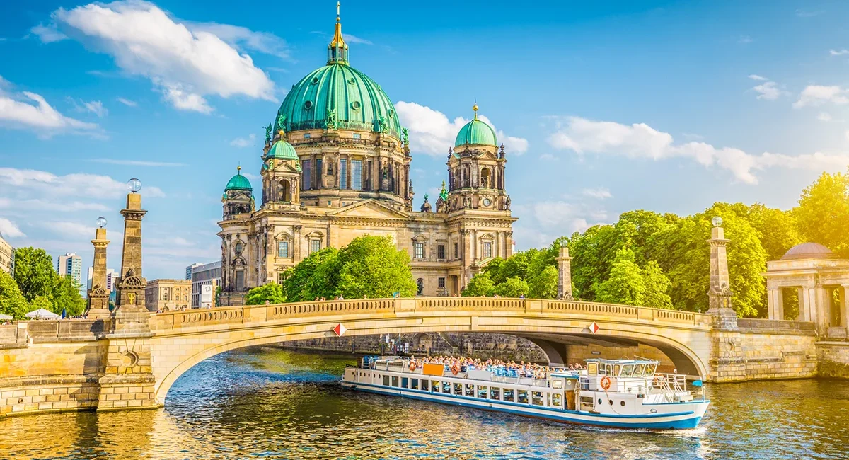 Der majestätische Berliner Dom mit seiner markanten grünen Kuppel hinter der Schlossbrücke, während ein Ausflugsschiff auf der Spree vorbeifährt.