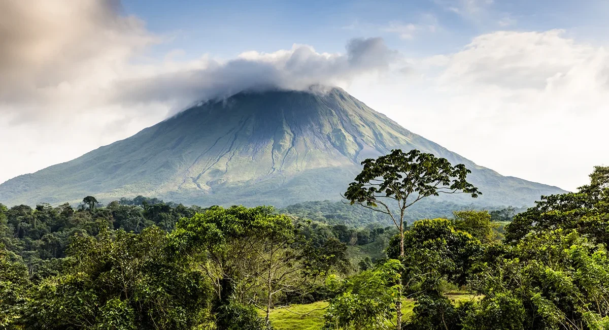 Der Vulkan Arenal erhebt sich kegelförmig über der grünen Landschaft Costa Ricas. Umgeben von Regenwald und Wolken dominiert der markante Vulkan die Szenerie.