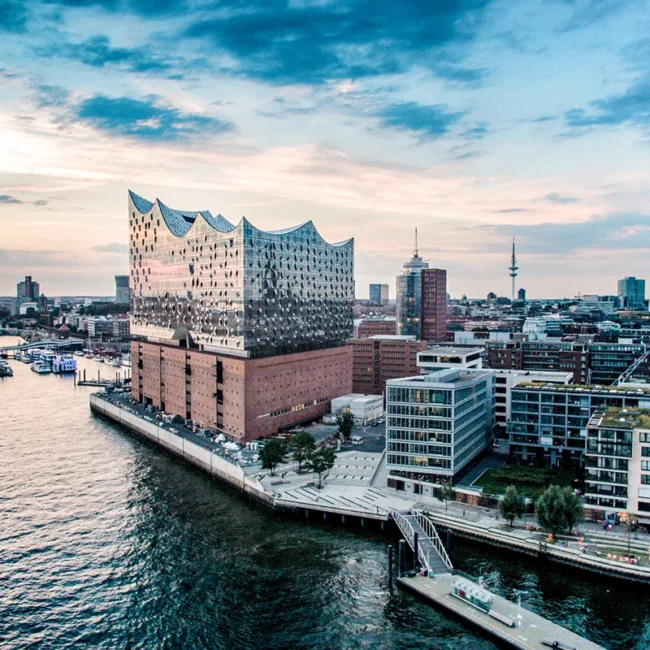 Die Elbphilharmonie in Hamburg steht am Ufer der Elbe. Das moderne Glasgebäude mit wellenförmigem Dach sitzt auf einem historischen Backsteinspeicher im Hafen.