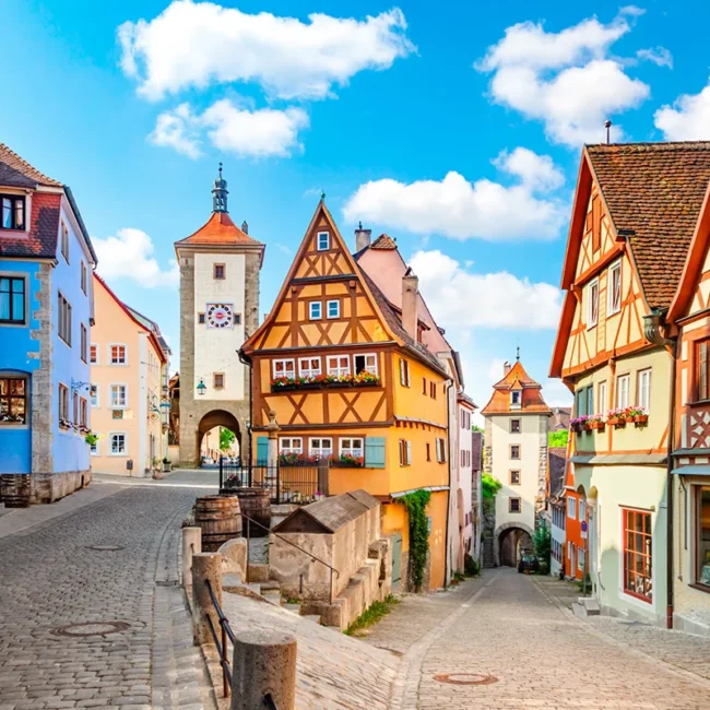 Das Plönlein in Rothenburg ob der Tauber, ein ikonisches gelbes Fachwerkhaus an einer Straßengabelung, das von mittelalterlichen Türmen und Kopfsteinpflaster eingerahmt wird.
