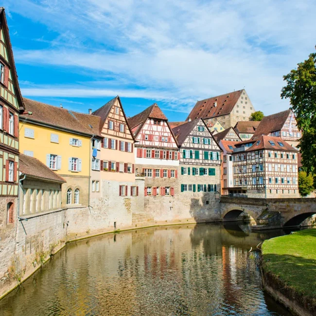 Eine Häuserzeile mit historischen Fachwerkhäusern in der Altstadt von Schwäbisch Hall, die sich im ruhigen Wasser des Flusses Kocher spiegelt.