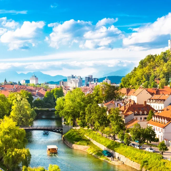 Die malerische Altstadt von Ljubljana am Ufer des Flusses Ljubljanica, über der das historische Schloss auf einem grünen Hügel thront.