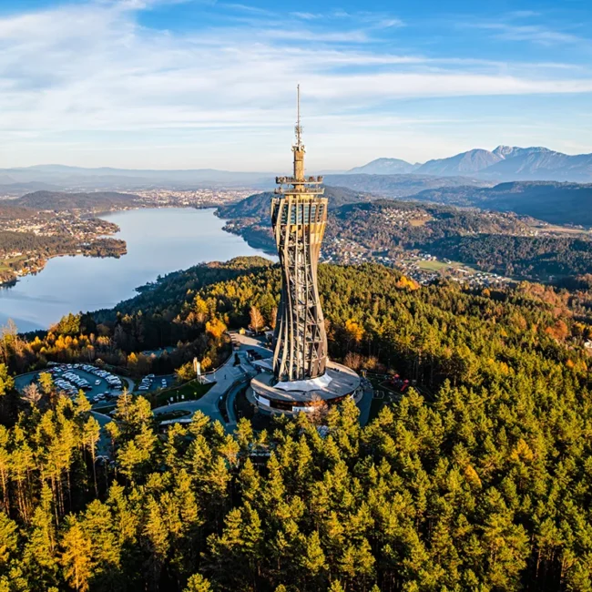 Der Aussichtsturm Pyramidenkogel, der als markante Holzkonstruktion inmitten bewaldeter Hügel über dem glitzernden Wörthersee in Kärnten thront.