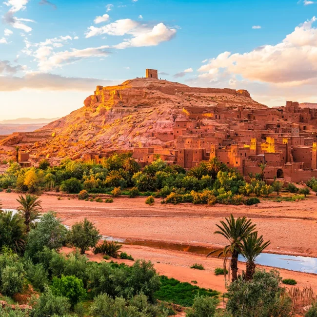 Die Wüstenstadt Ait Benhaddou in Marokko besteht aus traditionellen Lehmhäusern, die sich an einem Hügel in der trockenen Landschaft entlangziehen.