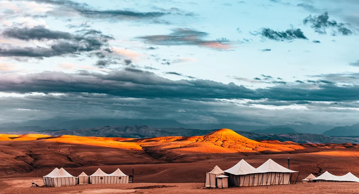 Ein Wüstencamp in der marokkanischen Sahara mit mehreren Zelten zwischen hohen Sanddünen. Die Zelte stehen in der weiten Wüstenlandschaft unter dem offenen Himmel.