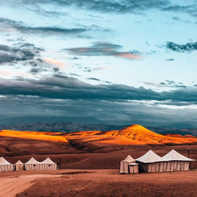 Ein Wüstencamp in der marokkanischen Sahara mit mehreren Zelten zwischen hohen Sanddünen. Die Zelte stehen in der weiten Wüstenlandschaft unter dem offenen Himmel.