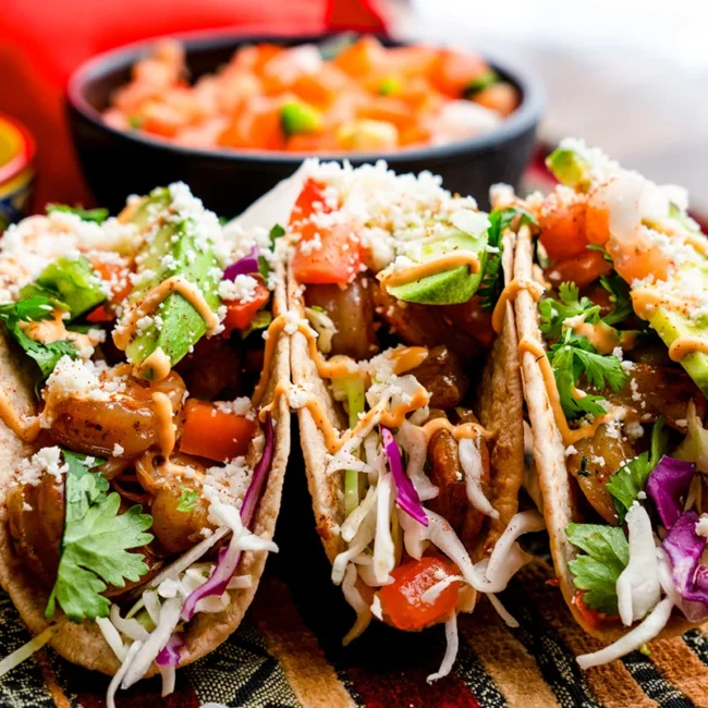 Drei Tacos liegen auf einem Teller. Die gefüllten Tortillas sind mit verschiedenen Zutaten belegt und typisch für die mexikanische Küche.