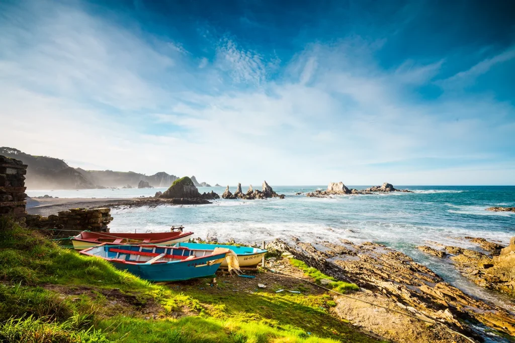Mehrere Boote liegen an Land an einer steinigen Küste in Nordspanien, nahe dem Meer.