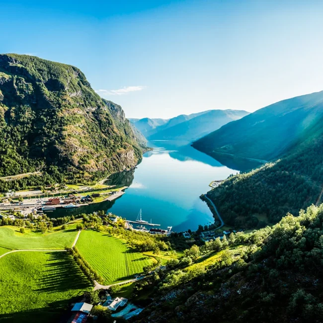 Der Aurlandsfjord in Norwegen liegt im Sonnenschein zwischen hohen Bergen. Das ruhige Wasser des Fjords spiegelt die umliegende Landschaft.