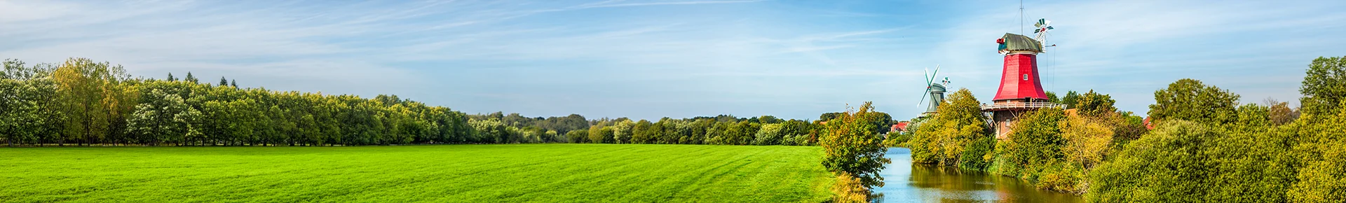 Die Greetsieler Zwillingsmühlen, die inmitten einer grünen Marschlandschaft direkt an einem malerischen Wasserlauf in Ostfriesland stehen.