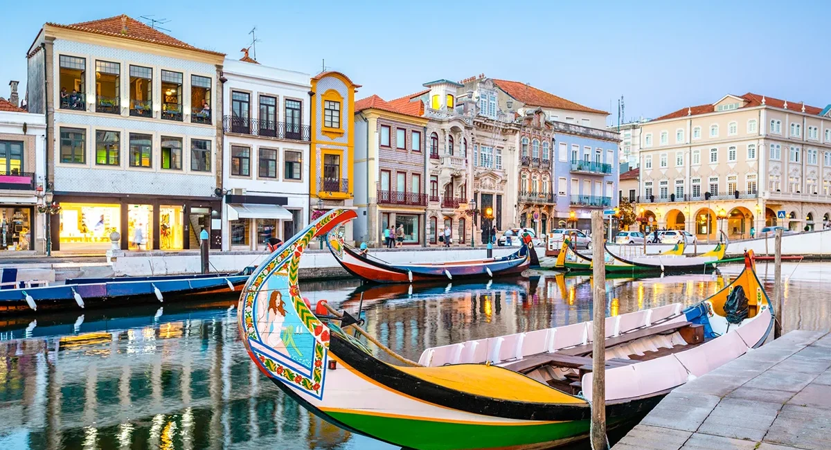 Bunte Moliceiro-Boote fahren durch einen Kanal in Aveiro in Portugal. Die traditionellen Boote liegen auf dem Wasser zwischen Häusern am Ufer.