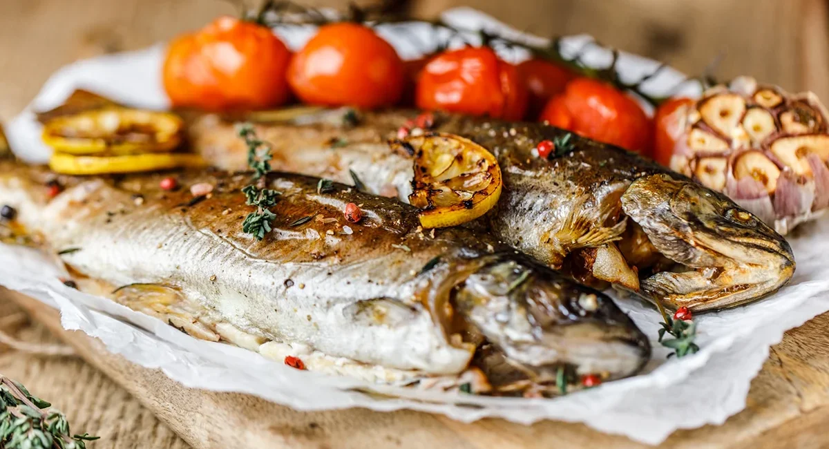 Ein gegrillter Fisch liegt auf einem Teller und wurde über offenem Feuer zubereitet.