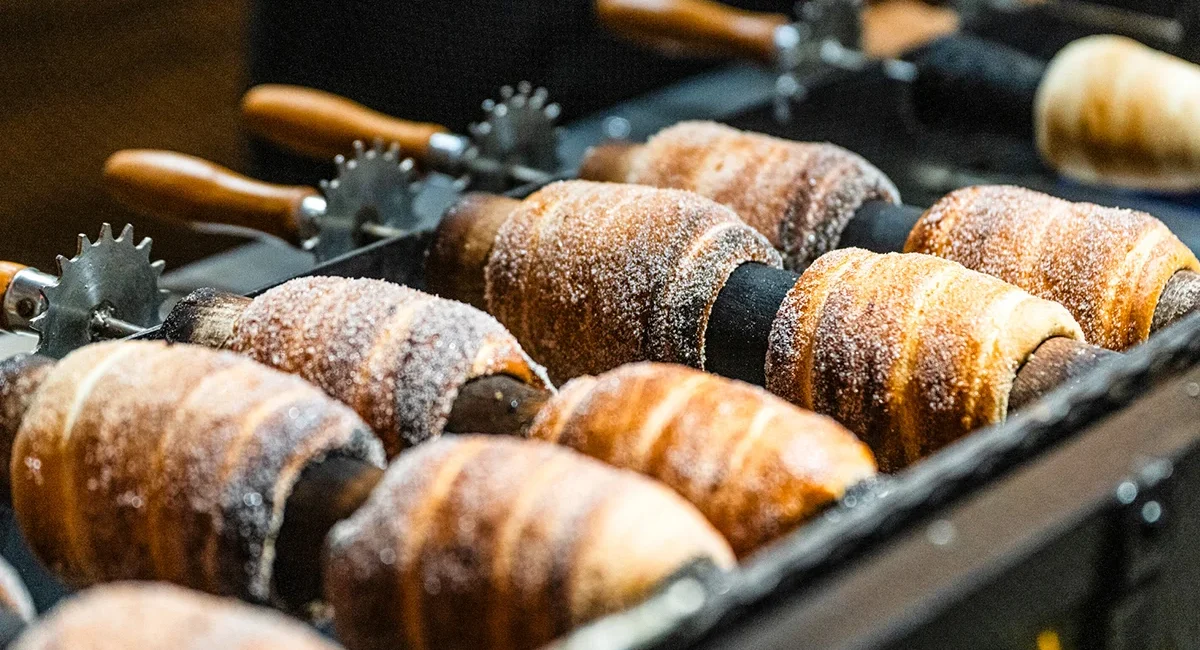 Trdelník (Baumstriezel) wird auf einem drehenden Zylinder über einem Grill gebacken.