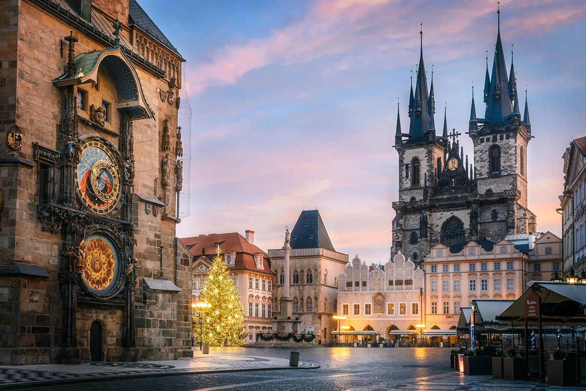 Ein großer Weihnachtsbaum steht auf dem Marktplatz in Prag und ist in der Abendstimmung festlich beleuchtet.