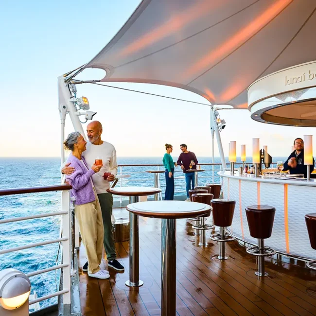 Auf der Lanai Bar auf dem AIDA-Schiff stehen zwei Paare auf dem Deck und trinken entspannt ihre Getränke.