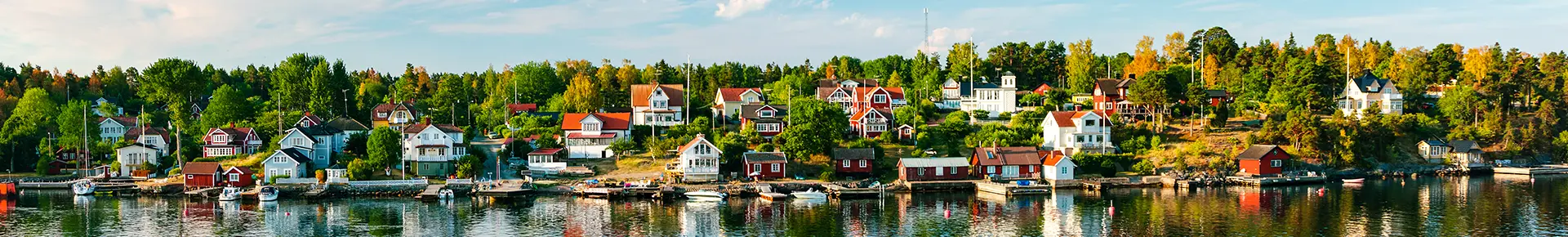 Blick vom Wasser auf die schwedische Schärenküste mit Felsen, vielen schwedischen Häusern und Bäumen am Ufer.