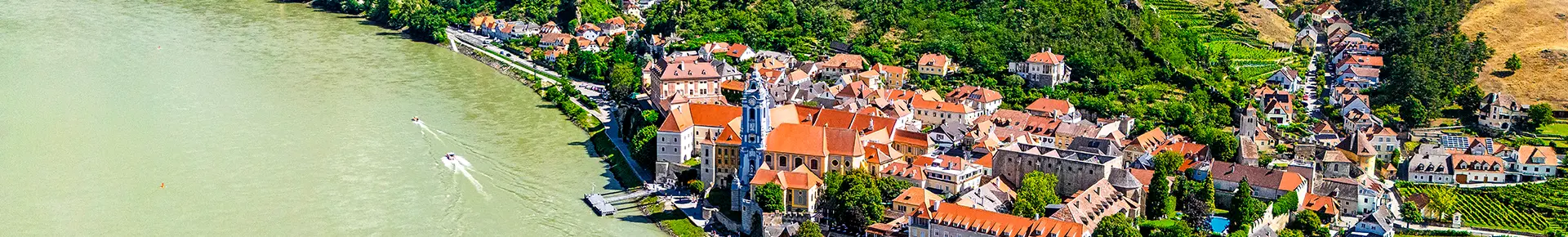 Blick von oben auf Dürnstein in der Wachau mit der Donau, der Altstadt und den Weinbergen.