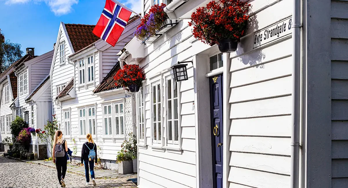 Eine Gasse in Stavanger mit weißen Holzhäusern, Blumentöpfen und einer norwegischen Flagge.