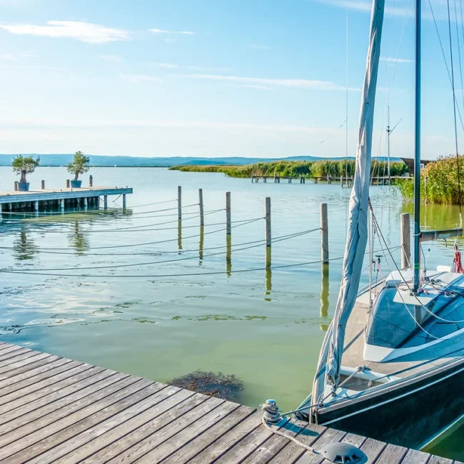 Ein Segelboot liegt an einem Holzsteg in einem modernen Hafen am Neusiedler See in Ungarn bei strahlendem Sonnenschein und angenehmer Atmosphäre.