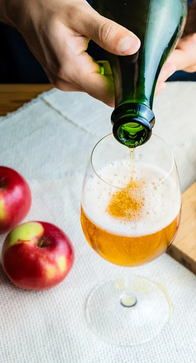 Goldener Apfelmost wird im Waldviertel aus einer dunklen Flasche in ein Weinglas eingeschenkt, während daneben zwei frische Äpfel liegen.