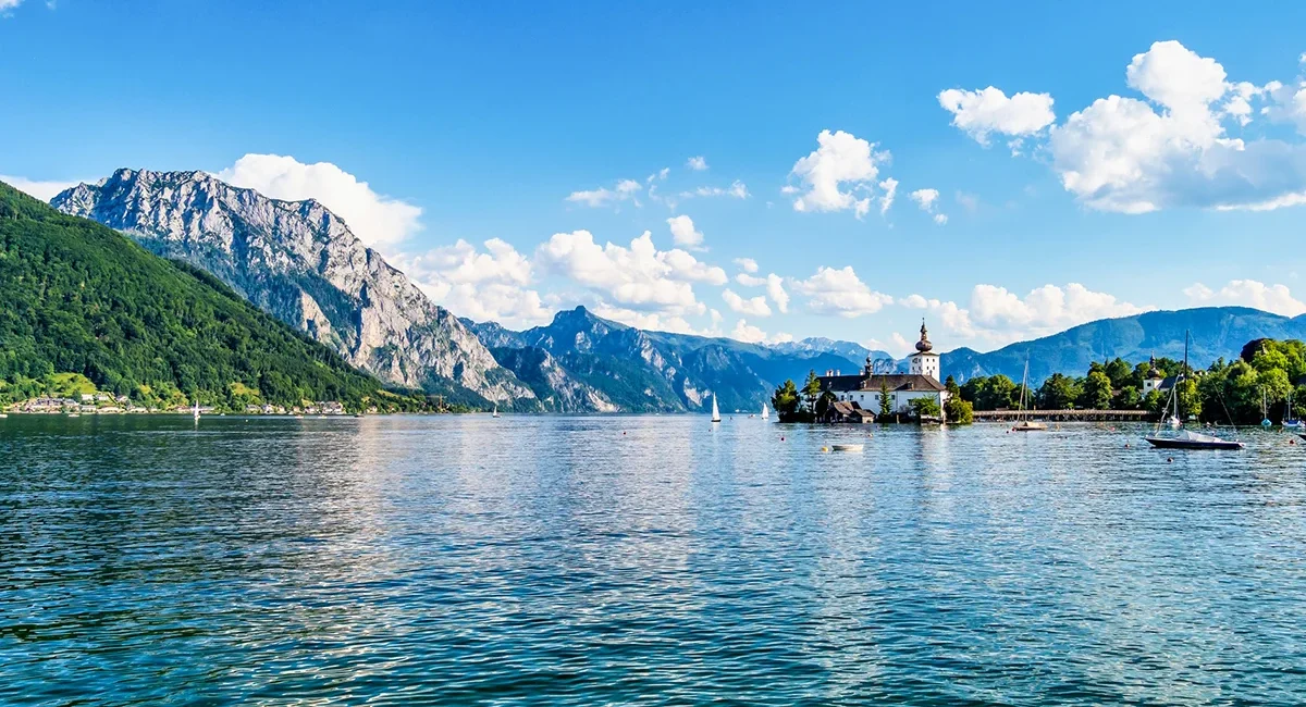 Das malerische Seeschloss Ort auf einer kleinen Insel im tiefblauen Traunsee, eingerahmt von der imposanten Bergkulisse des Salzkammerguts in Österreich.